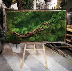 a moss covered canvas with trees and plants in the background on a wooden easel