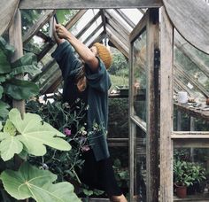 a woman standing in front of a green house holding her hand up to the sky