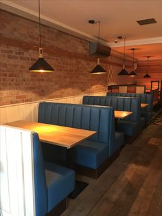 an empty restaurant with blue booths and wooden tables in front of a brick wall that has lights hanging from it