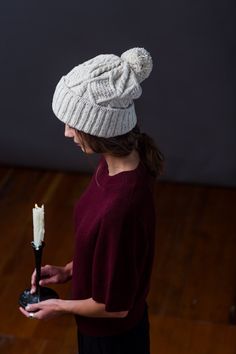 a woman holding a candle in her hand and wearing a knitted hat on top