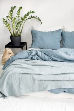 a bed with blue sheets and pillows in a room next to a potted plant