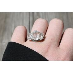 a person's hand holding an engagement ring with two diamonds on it and the middle one in white gold