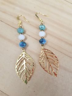 two gold leaf earrings with blue beads are sitting on top of a wooden table next to a