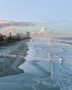 people are walking on the beach in front of an ocean and high rise cityscape