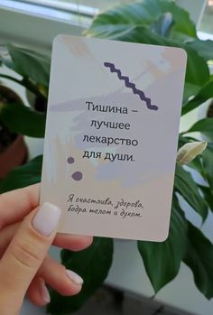 a person holding up a card with the words in russian and english on it next to a potted plant