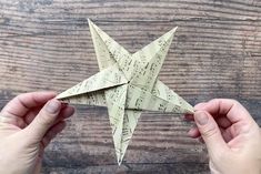 two hands holding an origami star on top of a wooden table with sheet music notes