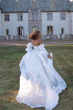 a woman in a white wedding dress is walking through the grass with her back to the camera