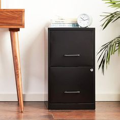 a black filing cabinet next to a wooden chair and potted plant on the floor