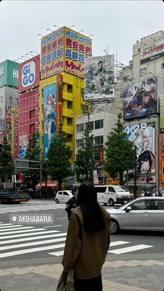 a woman walking across a cross walk in front of tall buildings with advertisements on them