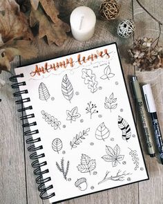 a notebook with autumn leaves on it next to a candle and some other items in front of it