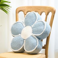 a blue flower pillow sitting on top of a wooden chair next to a potted plant