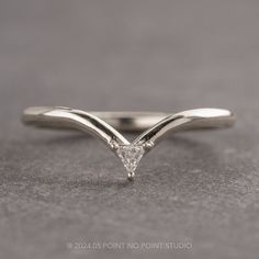 a white gold wedding band with a triangle shaped diamond in the center on a gray surface