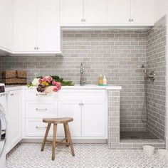 an image of a kitchen with white cabinets and grey tile on the walls, along with a small stool