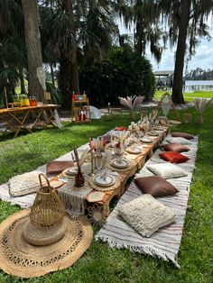 a long table set up with plates and place settings for dinner on the grass in front of some palm trees