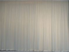 an empty room with white curtains on the wall