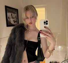 a woman taking a selfie in the bathroom with her cell phone and fur coat