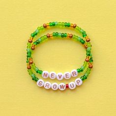 two beaded bracelets with the words never grow up on them, against a yellow background