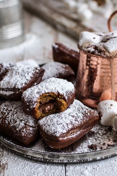 powdered sugar covered pastries on a plate next to a copper mug and cup