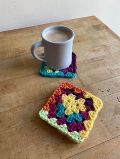 a cup of coffee sitting on top of a wooden table next to a crocheted coaster