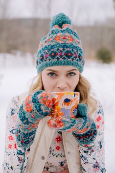 a woman holding a cup in her hands while wearing winter clothing and mittens