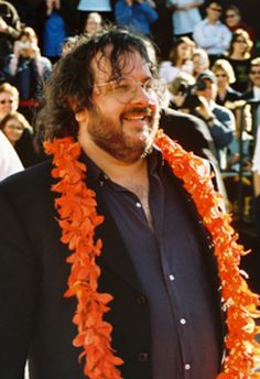 a bearded man with an orange lei around his neck and glasses on, standing in front of a crowd