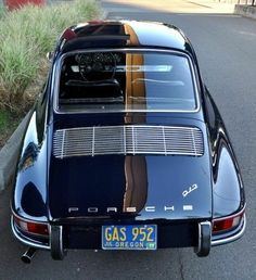 an old black car parked on the side of the road with its reflection in it's rear window