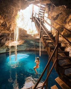 a woman hanging from a rope in the middle of a blue pool with stairs leading up to it