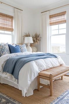 a bed with blue and white comforter in a bedroom next to two large windows