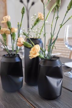 three black vases with flowers in them on a table