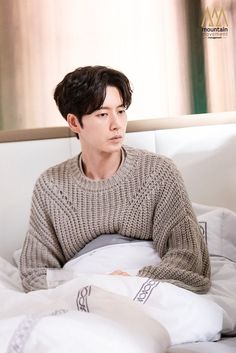 a young man sitting on top of a bed next to pillows and pillowcases