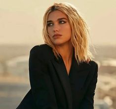 a woman with blonde hair and black blazer posing for a photo on top of a building