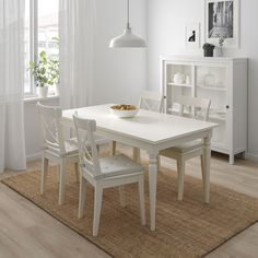 a white dining table with chairs and a bowl of fruit on the table next to it