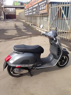 a motor scooter parked in front of a fenced off area with signs on it