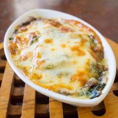 a casserole dish with cheese and vegetables in it sitting on a wooden tray