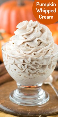 pumpkin whipped cream in a glass bowl on top of a wooden board with an orange pumpkin behind it