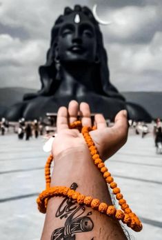 a person with a tattoo on their arm holding up a beaded bracelet in front of a buddha statue