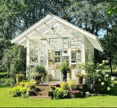 a small white house sitting in the middle of a lush green field with lots of flowers