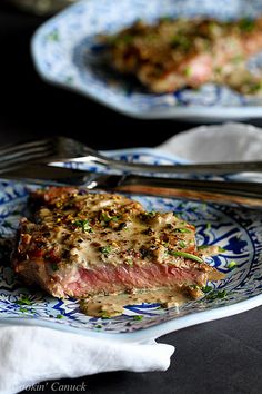 a piece of steak on a blue and white plate with a fork next to it