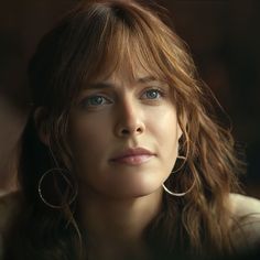 a close up of a person with long hair and blue eyes wearing large hoop earrings