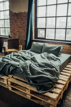 a bed made out of wooden pallets in a room with large windows and brick walls