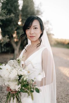 a woman in a white dress holding a bouquet of flowers and wearing a wedding veil