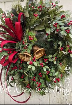 a christmas wreath with bells, holly and red ribbon hanging on a white wooden wall