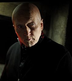 a bald man in a black jacket looking at the camera with an intense look on his face