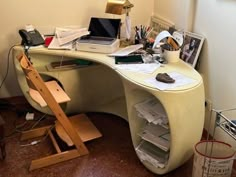 a desk with many items on it and a chair next to it in front of a window