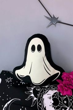 a black and white pillow with a ghost face on it next to a pink flower