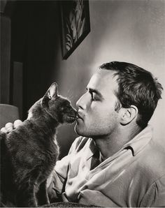 a man is kissing a cat on the nose while sitting in front of a lamp