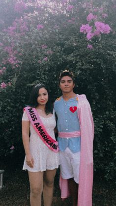 a man and woman dressed in costumes standing next to each other with flowers behind them