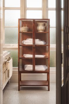 a wooden cabinet filled with white towels next to a window