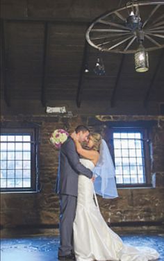 a bride and groom standing together in an old room with exposed ceiling beams, windows and chandelier