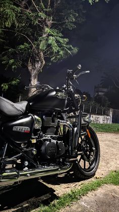 a black motorcycle parked on the side of a dirt road next to a tree at night